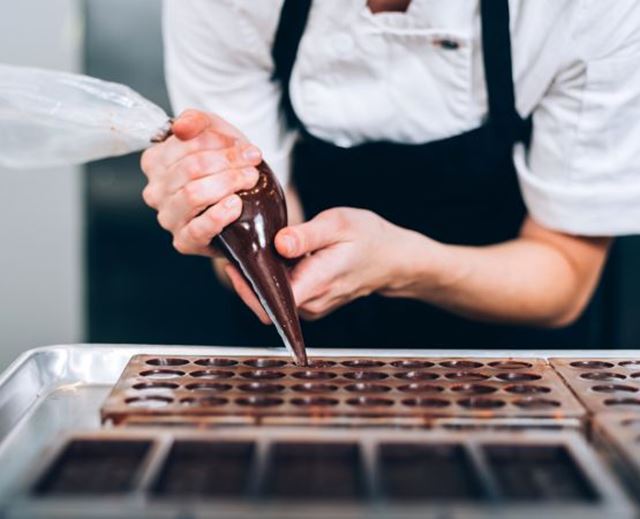 Artisan chocolatier remplissant un moule à chocolats avec une poche à douille en laboratoire