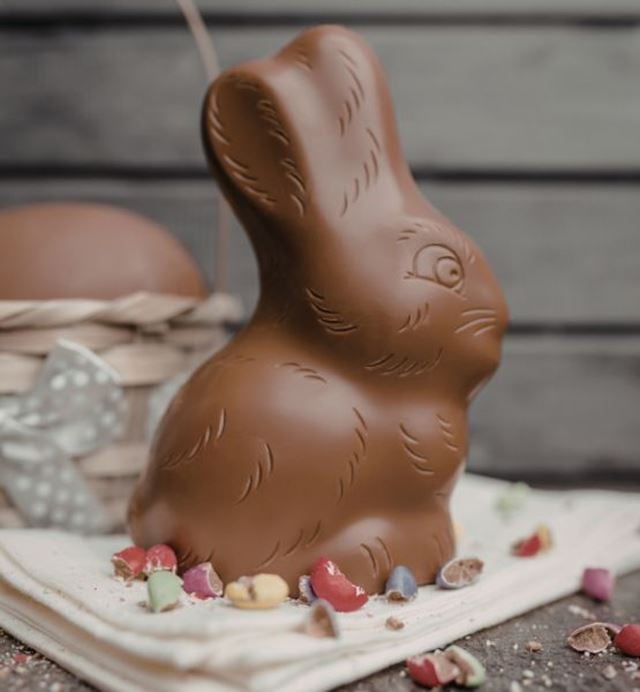 Lapin de Pâques en chocolat au lait posé sur un linge avec éclats de coquilles d’œufs colorées