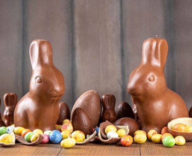 Lapins en chocolat au lait entourés d'œufs de Pâques colorés sur table en bois