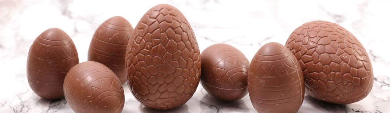 Assortment of milk chocolate Easter eggs with decorative patterns on white marble background