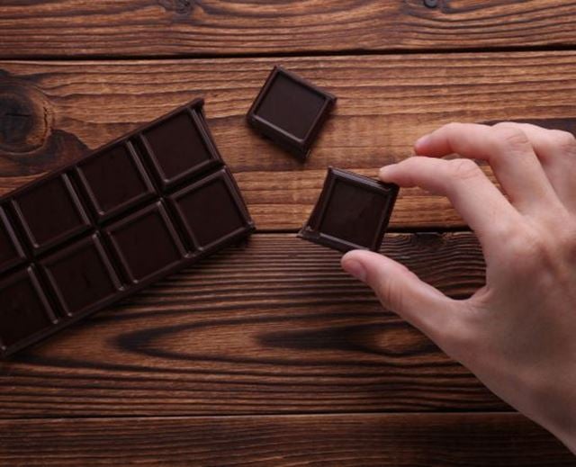 Main prenant un carré de chocolat noir sur une tablette posée sur une table en bois