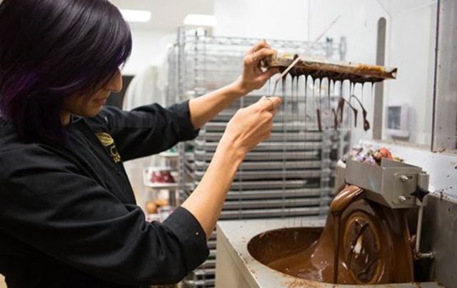 Un artisan chocolatier en train de verser ou manipuler du chocolat fondu sur une machine.
