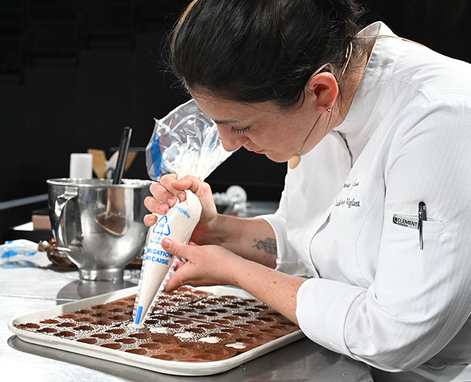 Cheffe en train de réaliser un geste pâtissier durant une démonstration live.