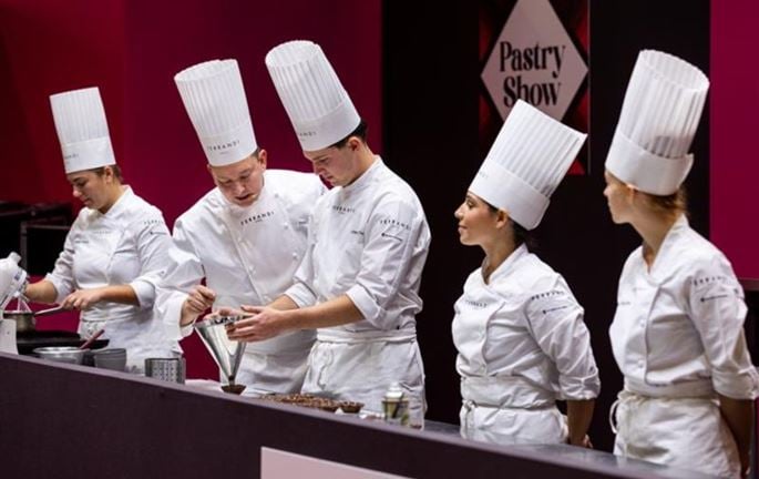 Pastry chefs in white uniforms preparing desserts on the Pastry Show stage at the Chocolate Show.